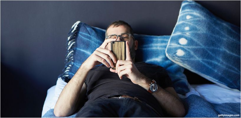 muž ležel na posteli a při pohledu na smartphone