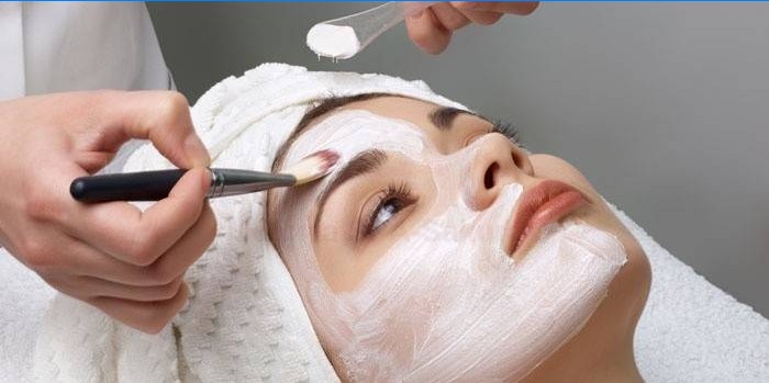 Kosmetička nanáší čisticí prostředky na obličej pacienta