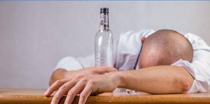 Opilý muž leží na stole a drží v ruce prázdnou láhev