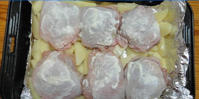 Kuřecí stehna na polštáři brambor před pečením na plech