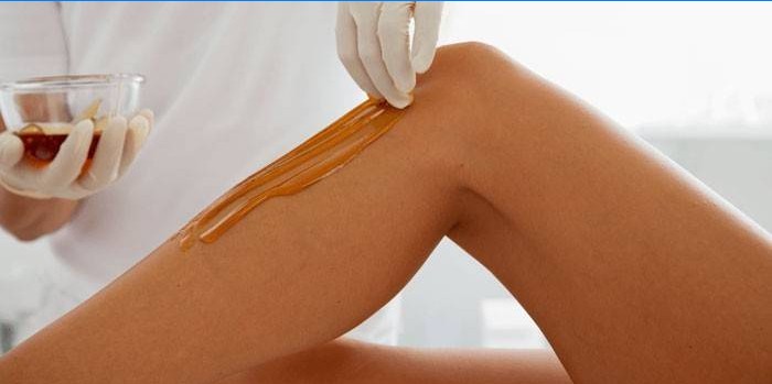 Kosmetička nanáší pastu na depilaci na kůži nohou.