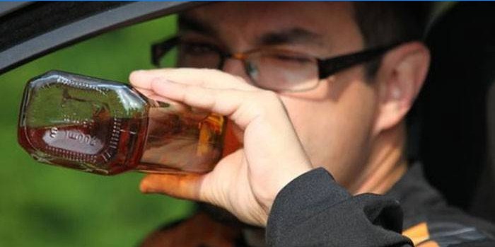 Muž v autě pije alkohol z láhve