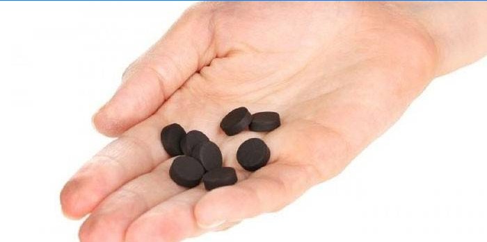Tablety z aktivního uhlí v dlani