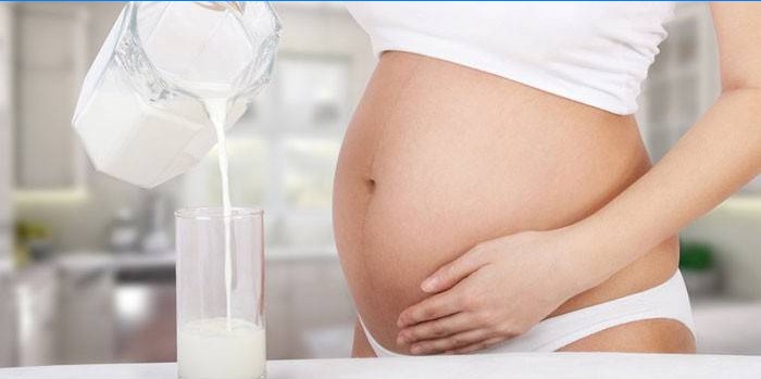 Těhotná žena nalévá fermentované pečené mléko do sklenice